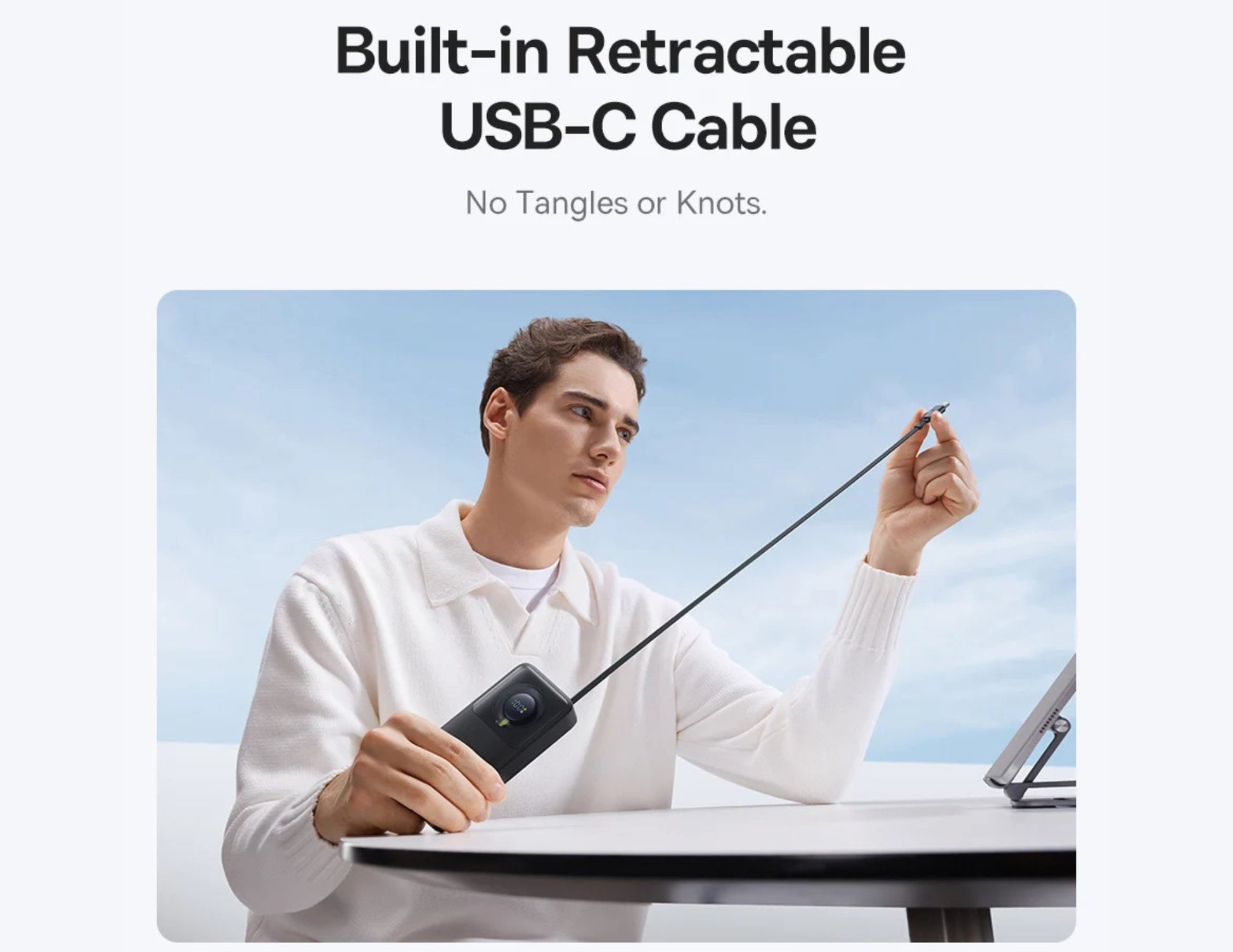 Person holding a phone with a retractable USB-C cable, set against a clear blue sky.