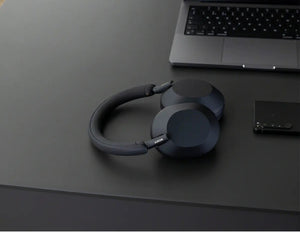 Black headphones on a dark surface with a laptop in the background
