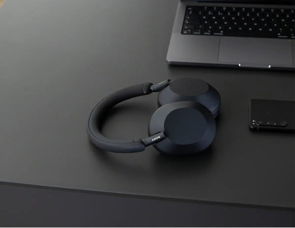 Black headphones on a dark surface with a laptop in the background
