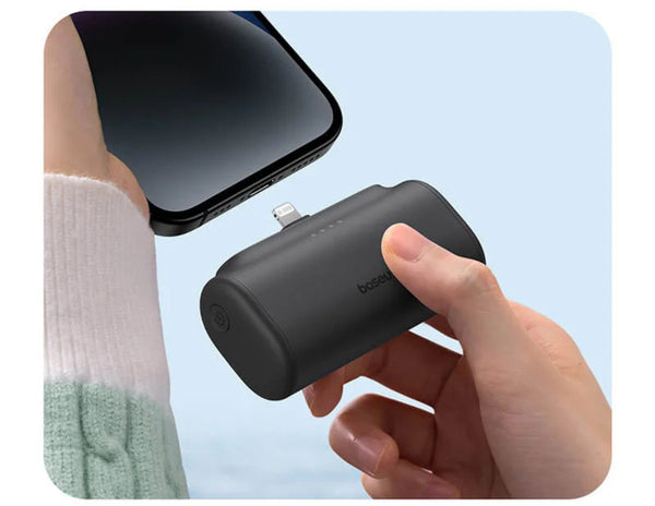 Hand holding a Baseus Compact Fast Charging Power Bank iP Edition with phone and person wearing green socks in the background