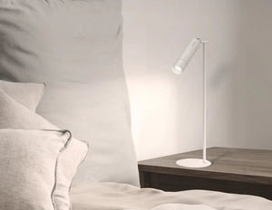 Momax SnapLux Portable LED Lamp QL12W on a wooden side table next to a bed with pillows.