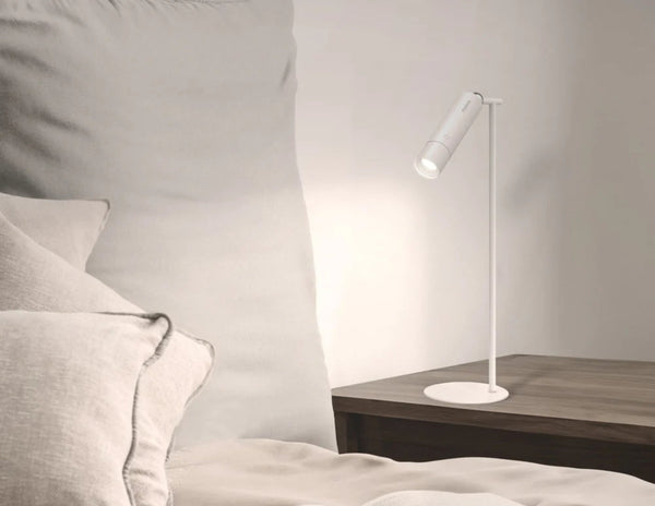Momax SnapLux Portable LED Lamp QL12W on a wooden side table next to a bed with pillows.