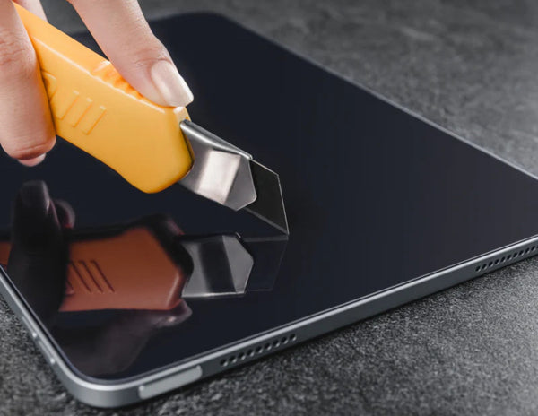 Person using a yellow utility knife to open a black smartphone.