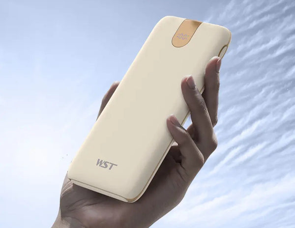 Beige wst power bank held in a hand with a sky background