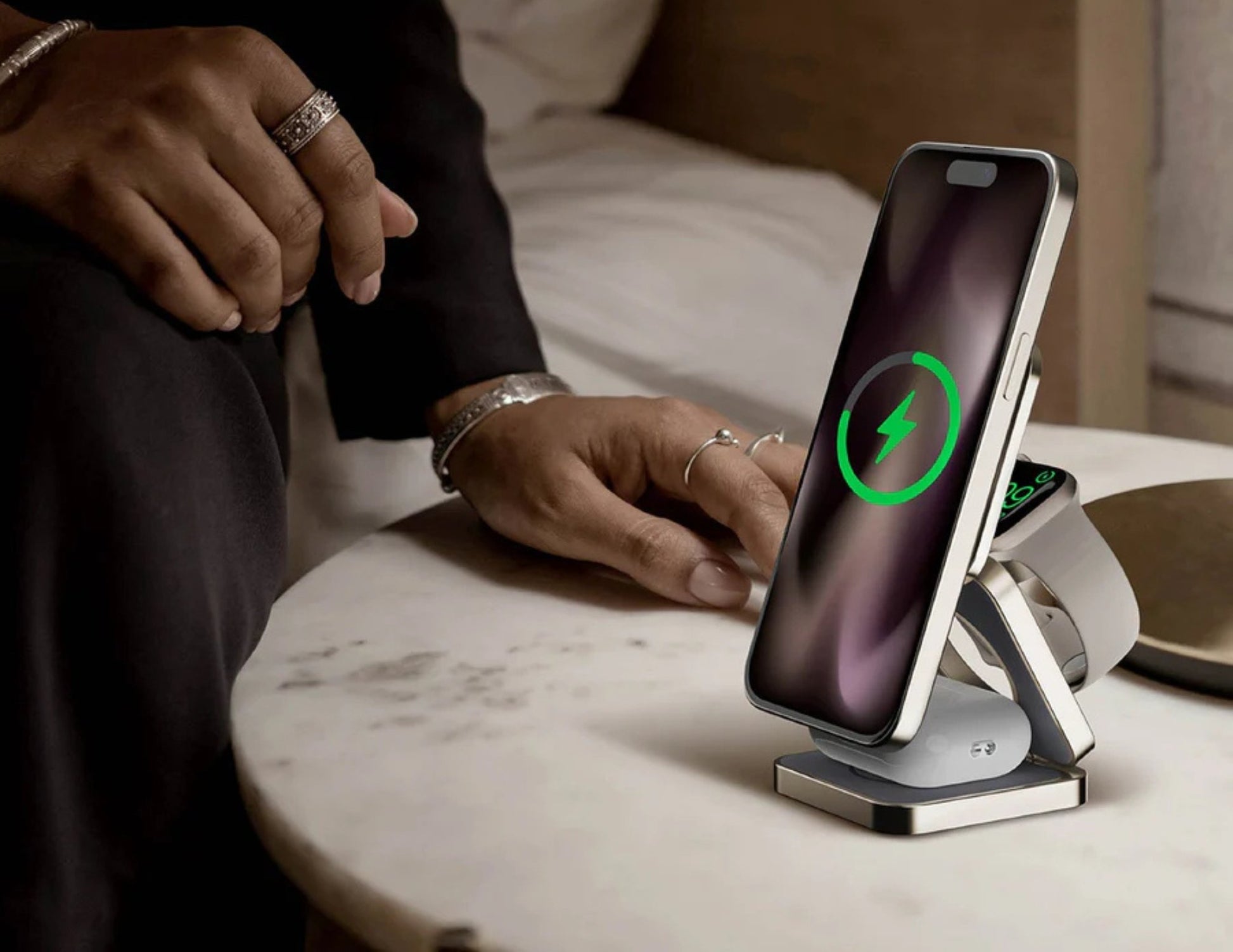 Person using a wireless charging stand with two devices on a marble surface.